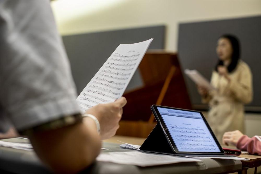 音乐系的学生一边在纸上和电脑上看着乐谱，一边听着教授在教室前面讲课.