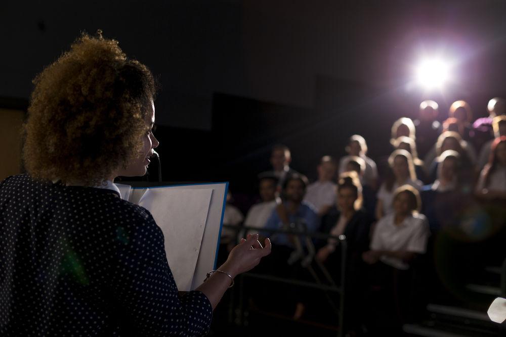 An actress holding a script is reciting lines in front of an audience.